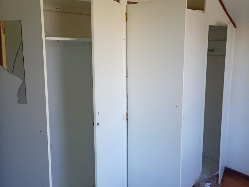 A bedroom featuring built-in cupboards, timber flooring, and a sloped ceiling, currently in need of maintenance and cosmetic updates.