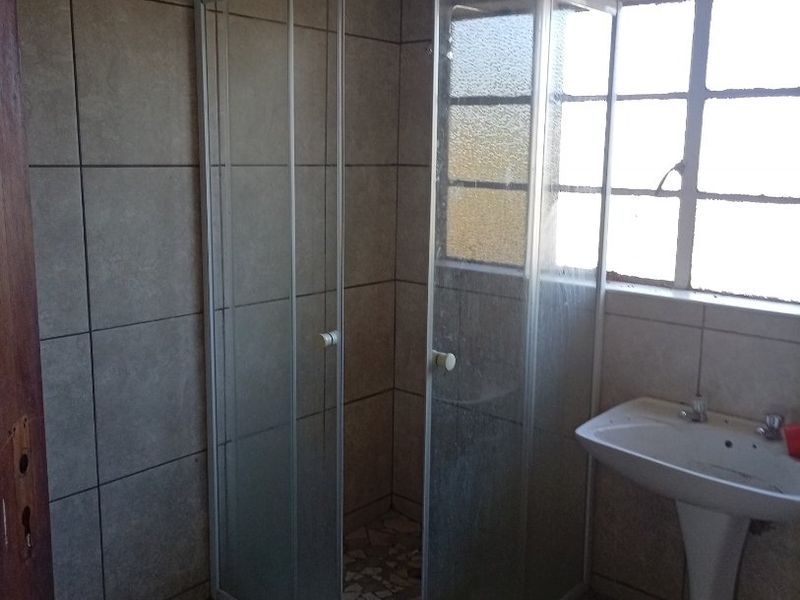 A functional bathroom featuring a corner shower enclosure, pedestal basin, and neutral wall and floor tiling.