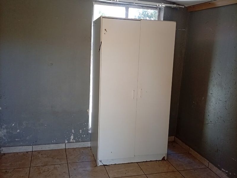A vacant bedroom featuring tiled flooring and a window, requiring cosmetic updates to the wall finishes and general maintenance.
