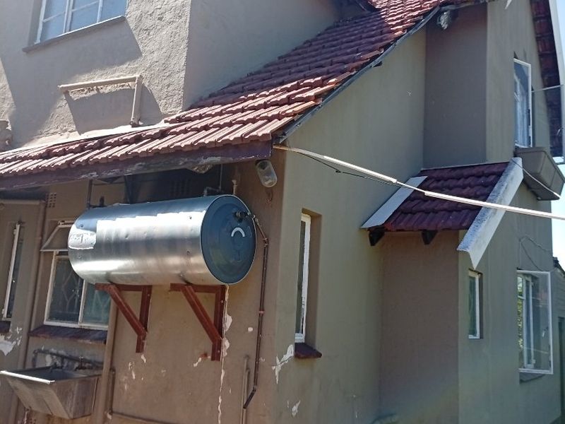 Rear exterior view of a two-story house featuring a mounted external geyser, utility sink, and tiled roof with visible signs of wear on the facade.