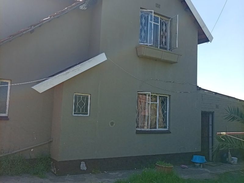 Rear elevation of a two-story house featuring a tiled roof, security-barred windows, and a concrete pathway surrounding the building base.