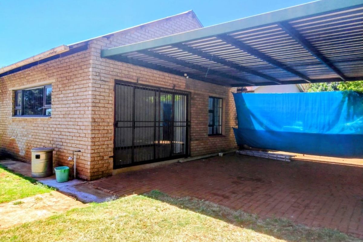 Rear exterior view of the property featuring a brick facade, a paved patio area, and a covered carport structure.