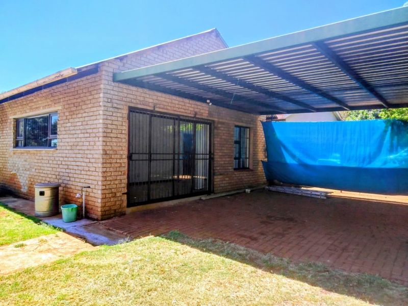 Rear exterior view of the property featuring a brick facade, a paved patio area, and a covered carport structure.