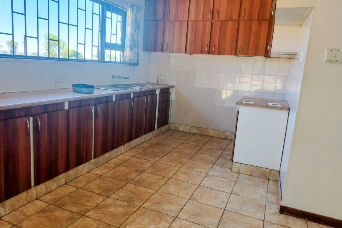 A functional kitchen featuring wood-look cabinetry, tiled flooring, a stainless steel sink, and a window with security bars.