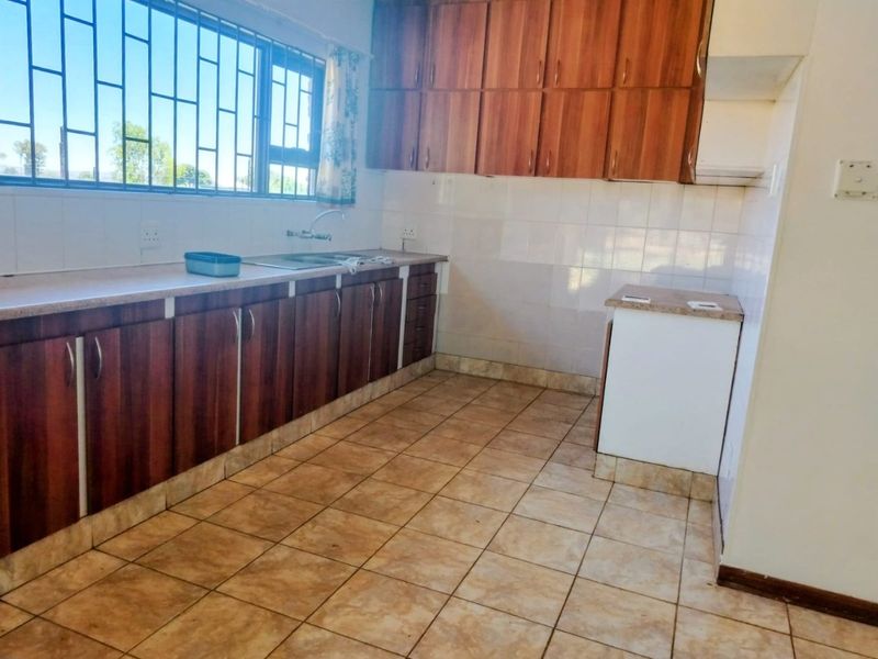 A functional kitchen featuring wood-look cabinetry, tiled flooring, a stainless steel sink, and a window with security bars.