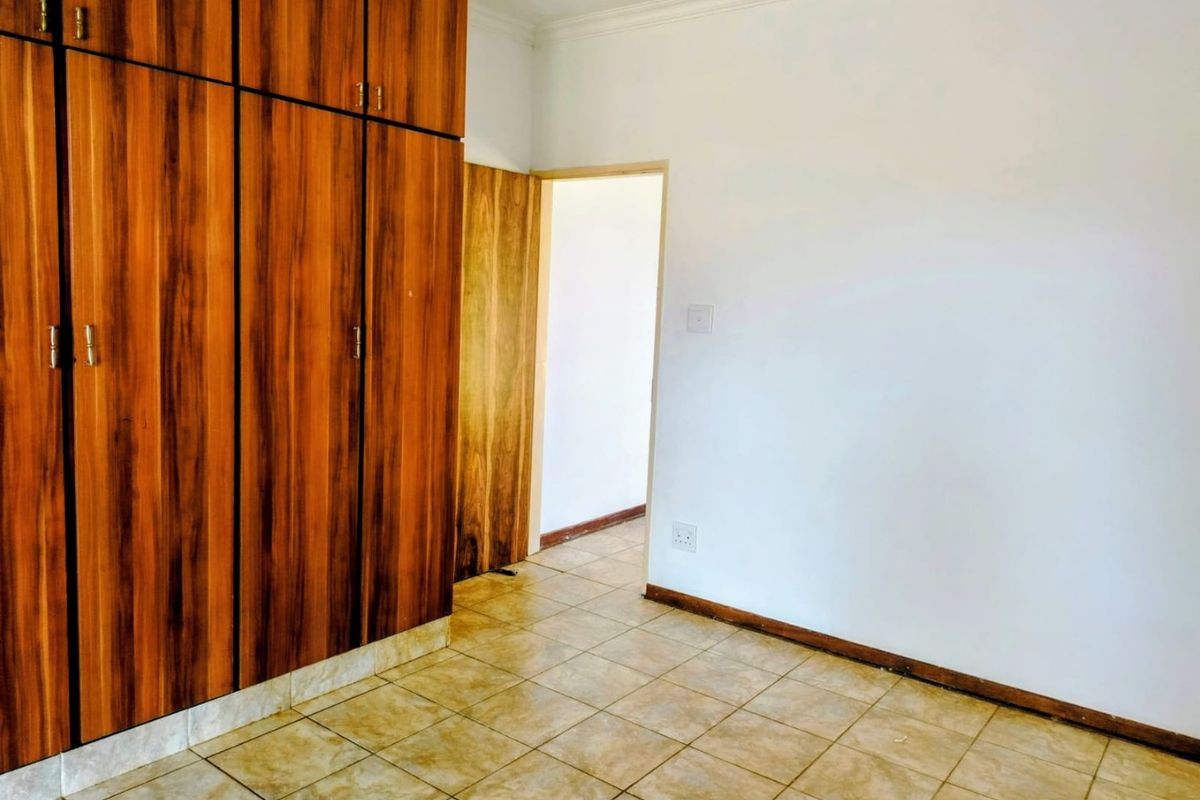 A vacant bedroom featuring built-in wooden cupboards, tiled flooring, and neutral walls, offering a clean canvas for personalization.