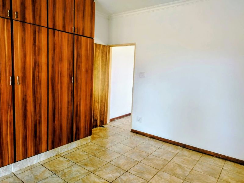 A vacant bedroom featuring built-in wooden cupboards, tiled flooring, and neutral walls, offering a clean canvas for personalization.