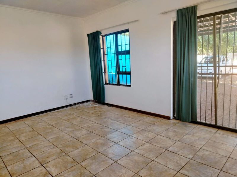 An empty living room featuring tiled flooring, a sliding glass door with security bars, and neutral walls, offering a blank canvas for interior design.