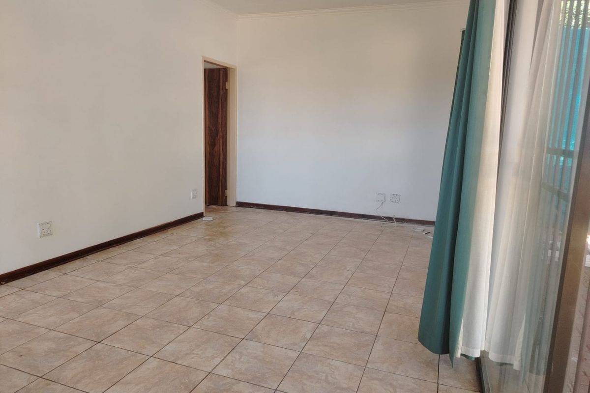 An empty, well-lit living area featuring neutral tiled flooring, clean white walls, and a sliding glass door providing access to the exterior.