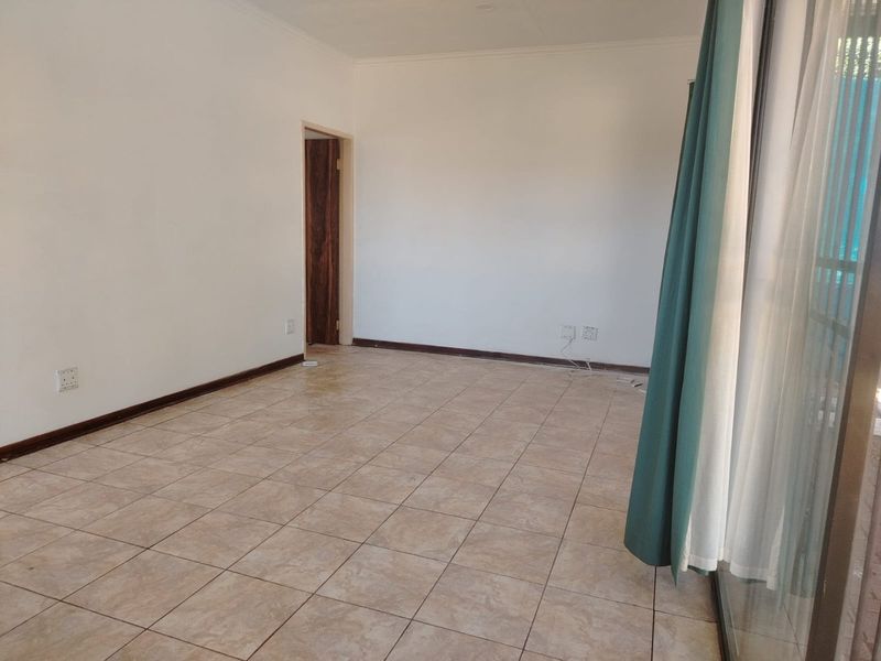 An empty, well-lit living area featuring neutral tiled flooring, clean white walls, and a sliding glass door providing access to the exterior.