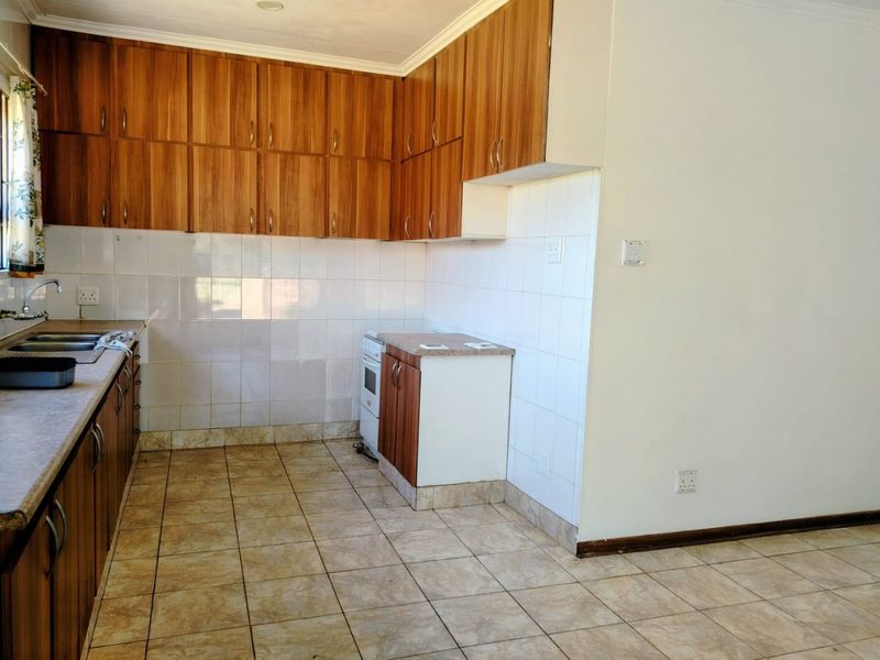 A functional kitchen featuring wood-look cabinetry, tiled backsplash, ceramic flooring, and a freestanding stove, offering a clean and practical layout.