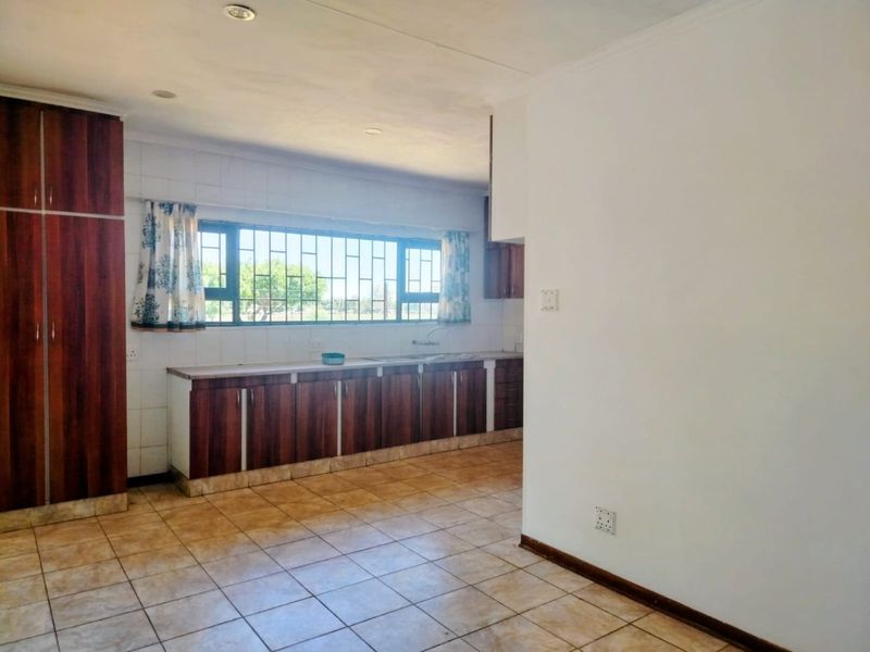 A functional kitchen featuring dark wood-look cabinetry, tiled flooring, and a large window with security bars, offering a clean and spacious layout.