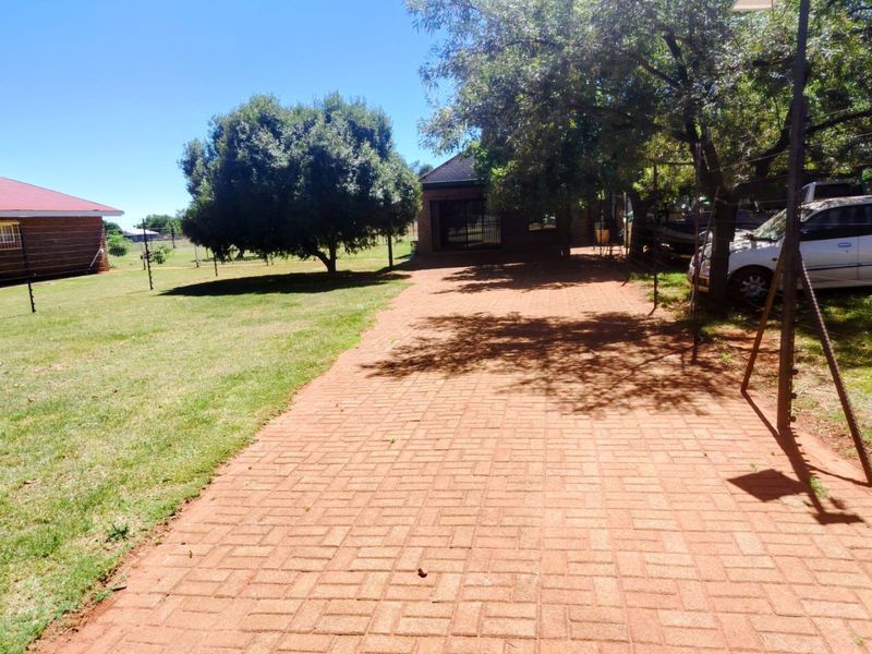 A view of the property entrance featuring a paved driveway, established trees, and perimeter electric fencing.