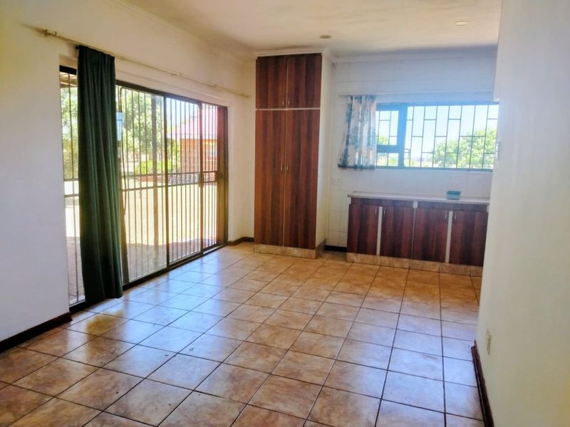 An open-plan living and kitchen area featuring tiled flooring, built-in cabinetry, and a sliding glass door with security bars leading to the exterior.
