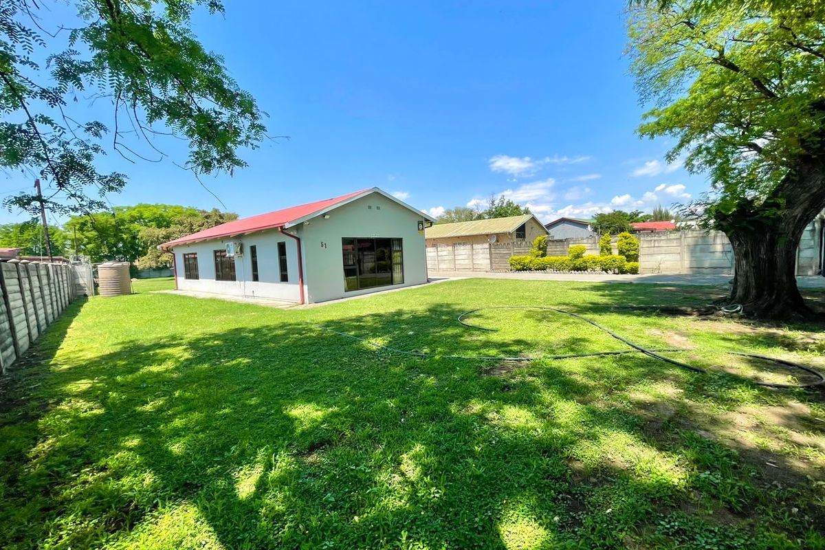 Spacious rear garden featuring a large lawn, mature trees, and a well-maintained house exterior with a metal roof and secure boundary walling.
