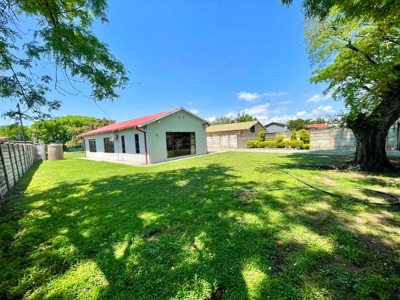 Spacious rear garden featuring a large lawn, mature trees, and a well-maintained house exterior with a metal roof and secure boundary walling.