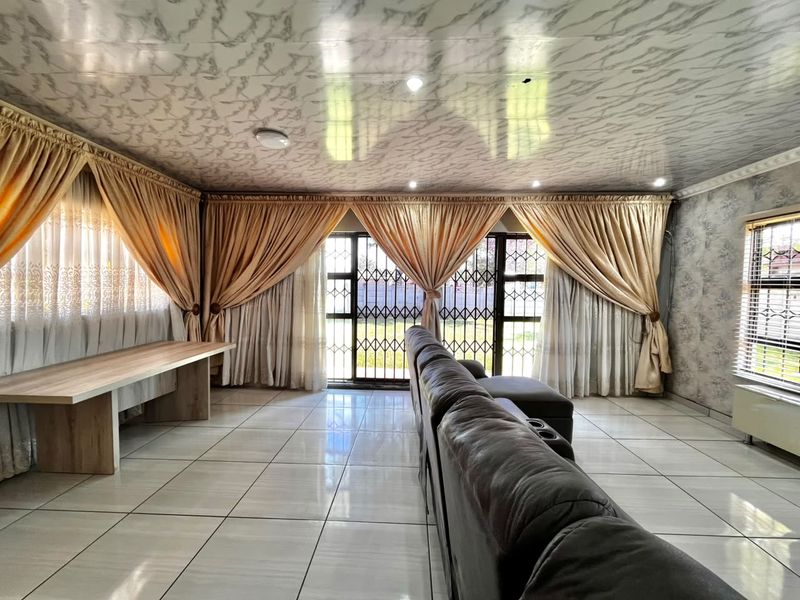 Spacious living room featuring tiled flooring, a patterned ceiling, and large windows with security gates, offering a bright and functional living space.