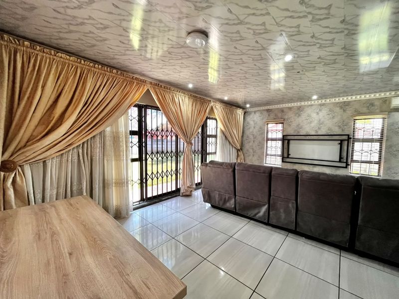 A living room featuring tiled flooring, decorative ceiling panels, and a sliding door with a security gate leading to the exterior.