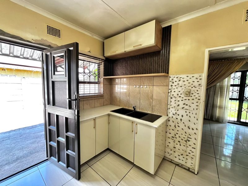 A compact kitchen area featuring built-in cabinetry, a double sink, and tiled finishes, requiring cosmetic updates to the surrounding wall surfaces.