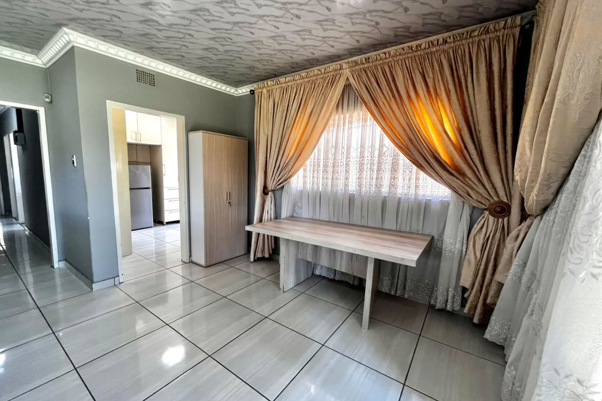 A living area featuring tiled flooring and decorative ceiling cornicing, with an open doorway leading to the kitchen area.