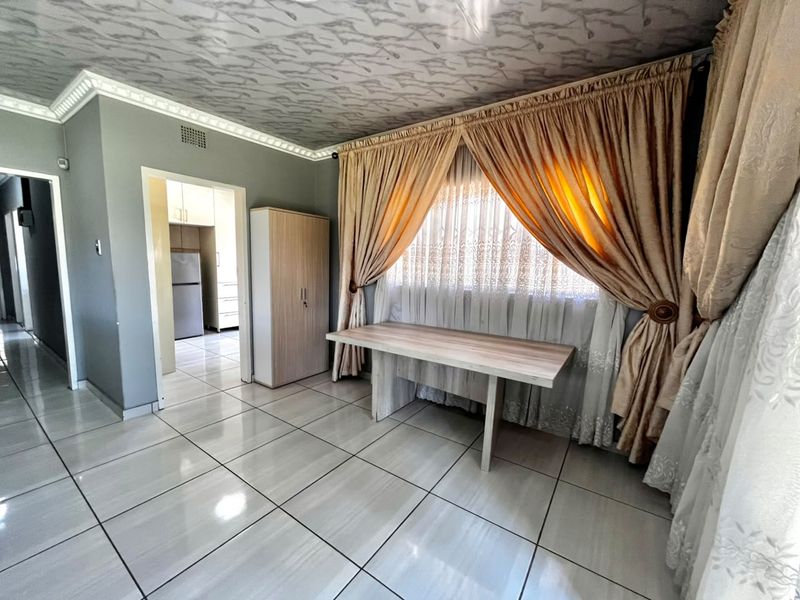 A living area featuring tiled flooring and decorative ceiling cornicing, with an open doorway leading to the kitchen area.