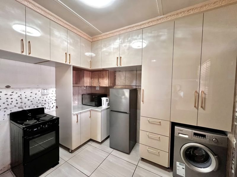 A compact kitchen featuring high-gloss cabinetry, tiled flooring, and integrated appliances, including a stove, oven, and washing machine.