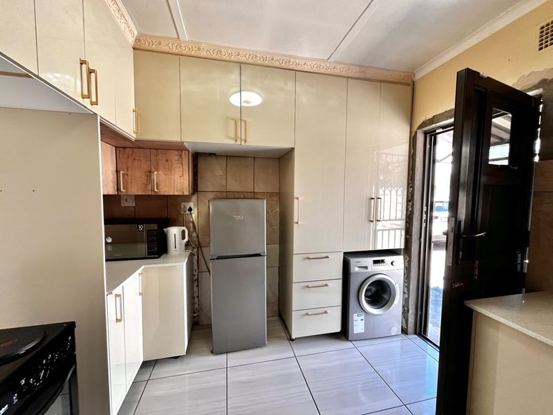 A functional kitchen featuring high-gloss cabinetry, tiled flooring, and a dedicated space for laundry appliances, with direct access to the exterior.