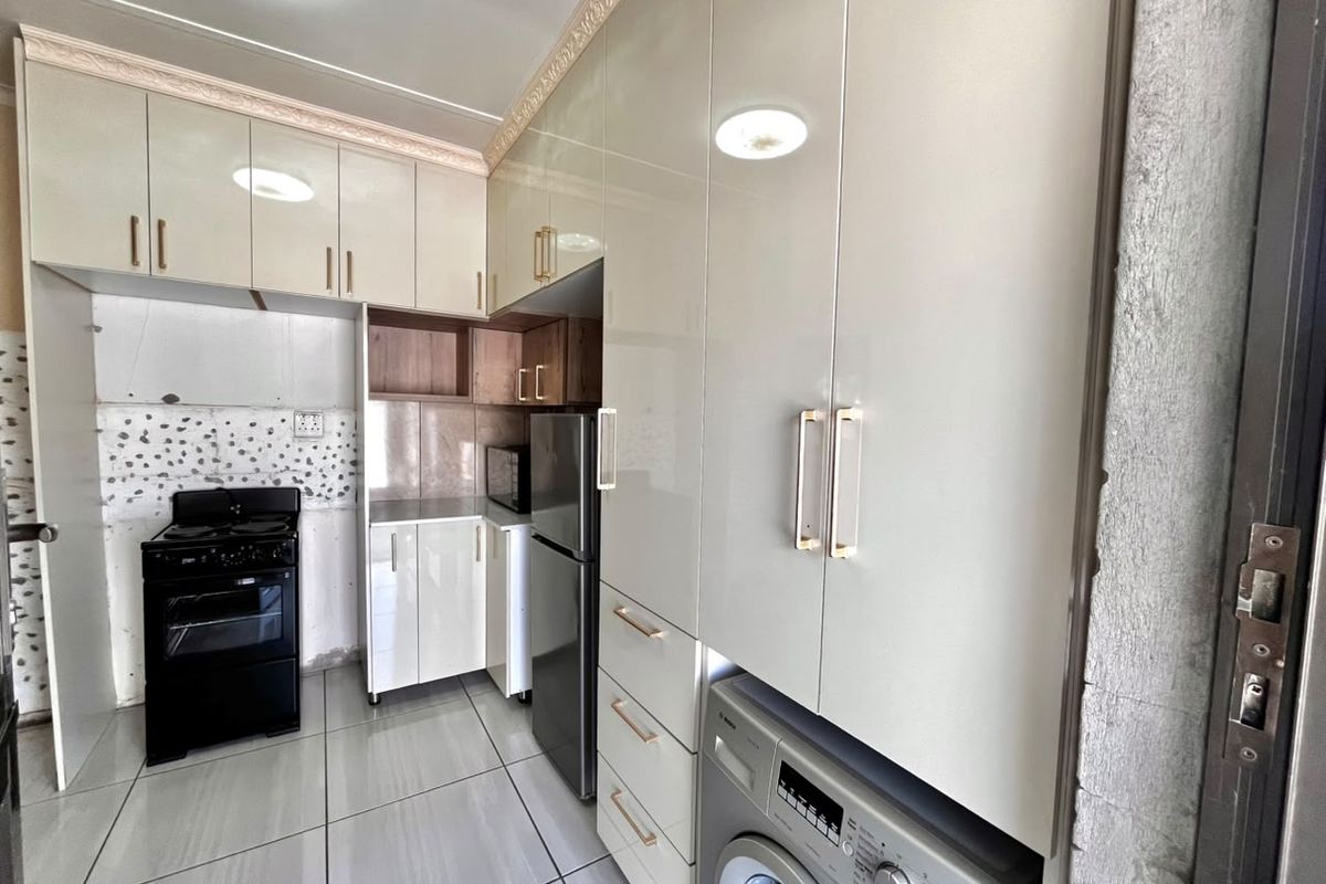 A functional kitchen featuring high-gloss cabinetry, tiled flooring, and integrated laundry appliances, with some areas requiring final finishing touches.