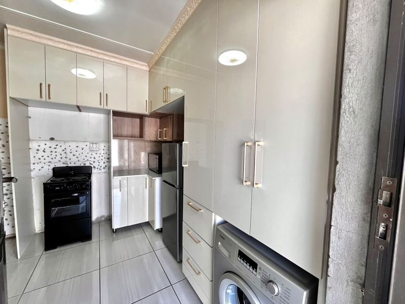 A functional kitchen featuring high-gloss cabinetry, tiled flooring, and integrated laundry appliances, with some areas requiring final finishing touches.