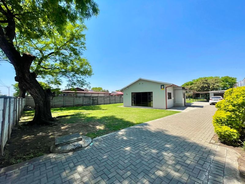 A view of the rear exterior featuring a paved driveway, a well-maintained lawn, and a precast concrete boundary wall.