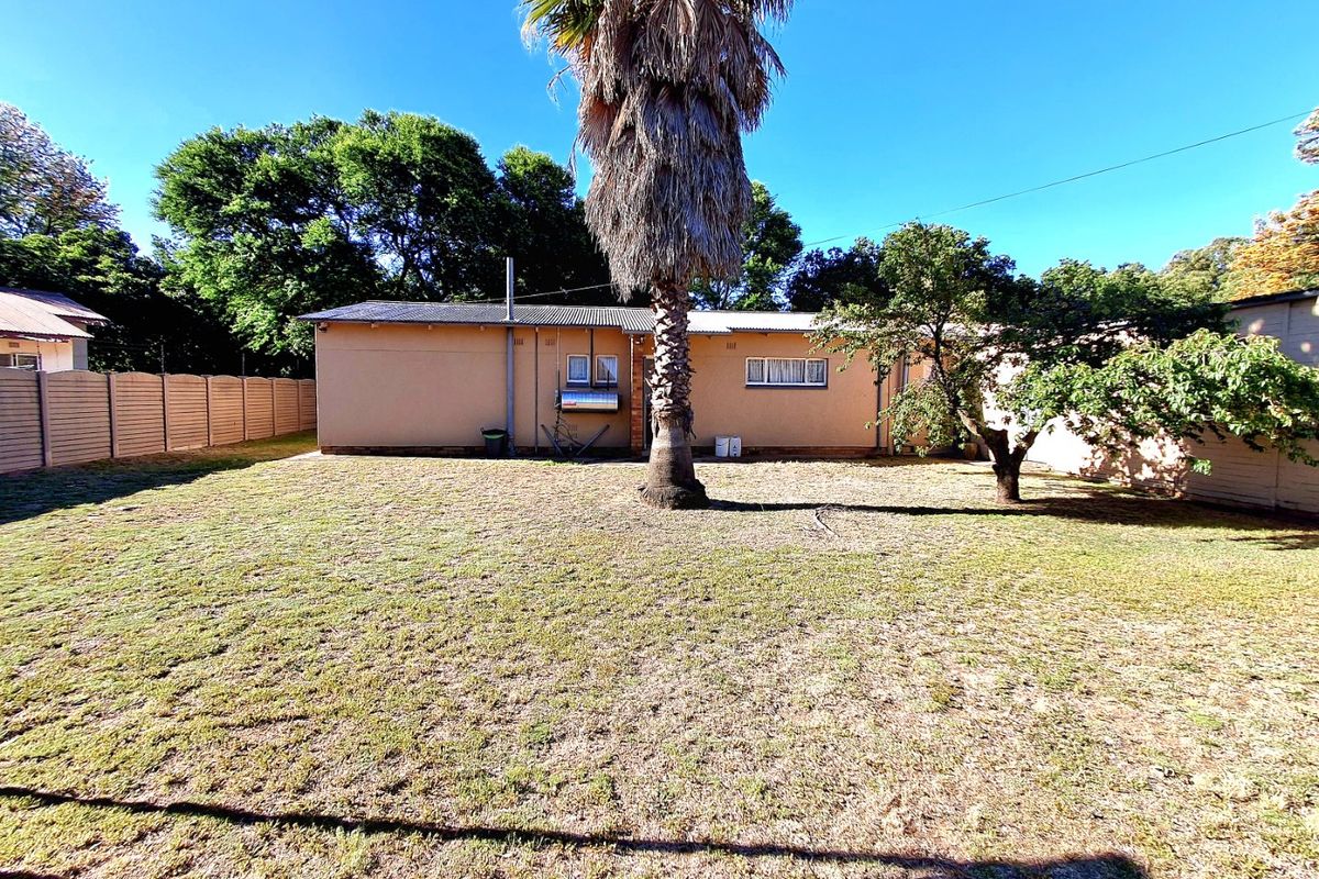 A view of the rear exterior of the house featuring a large lawn, mature palm tree, and a precast concrete boundary wall.