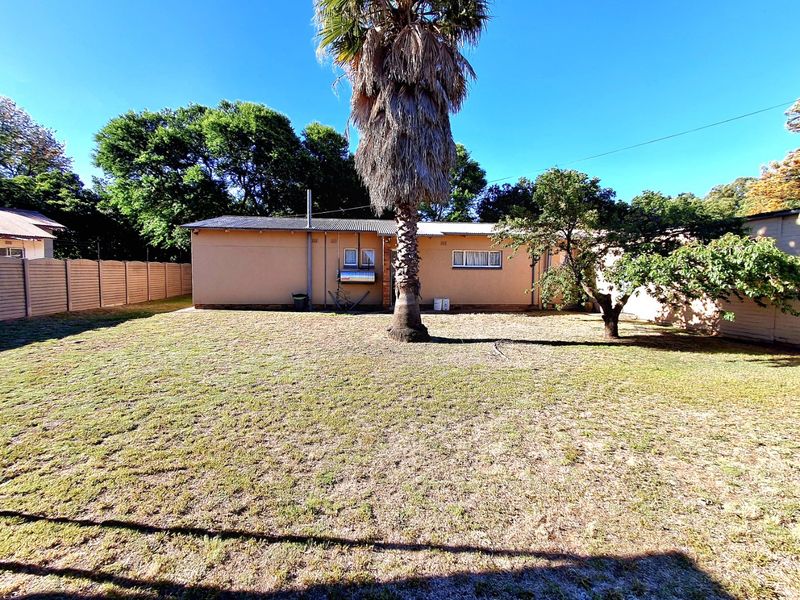 A view of the rear exterior of the house featuring a large lawn, mature palm tree, and a precast concrete boundary wall.