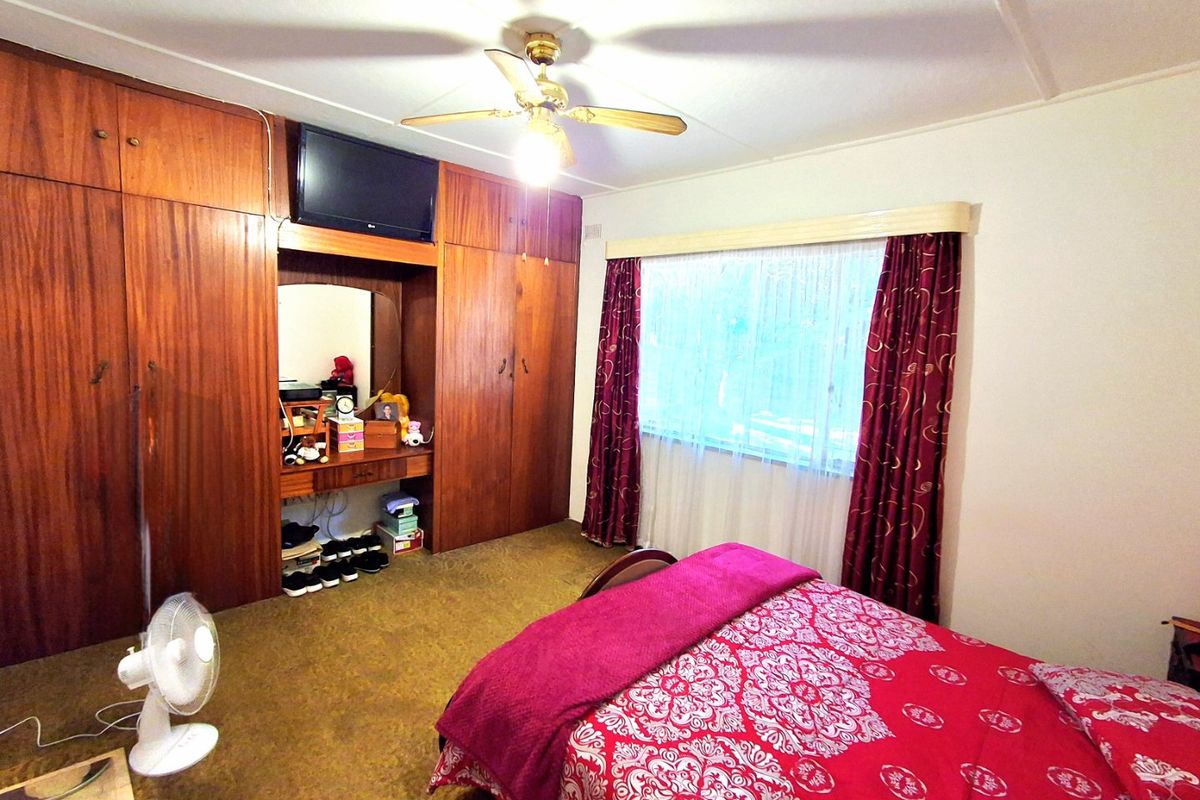 A bedroom featuring extensive built-in wooden cabinetry, a ceiling fan, and a window with a pelmet, offering potential for modernization.