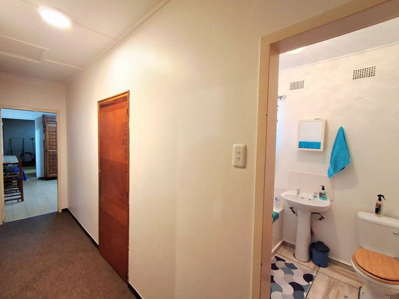 A functional hallway providing access to a bathroom featuring a pedestal basin and standard toilet, with neutral finishes throughout.