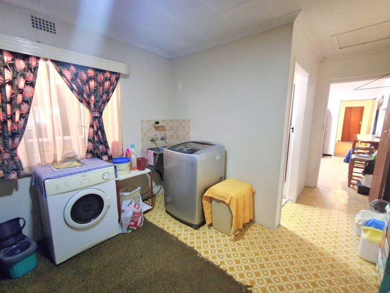 A functional laundry area featuring a wall-mounted sink, tiled splashback, and durable vinyl flooring, providing a practical space for household utility tasks.