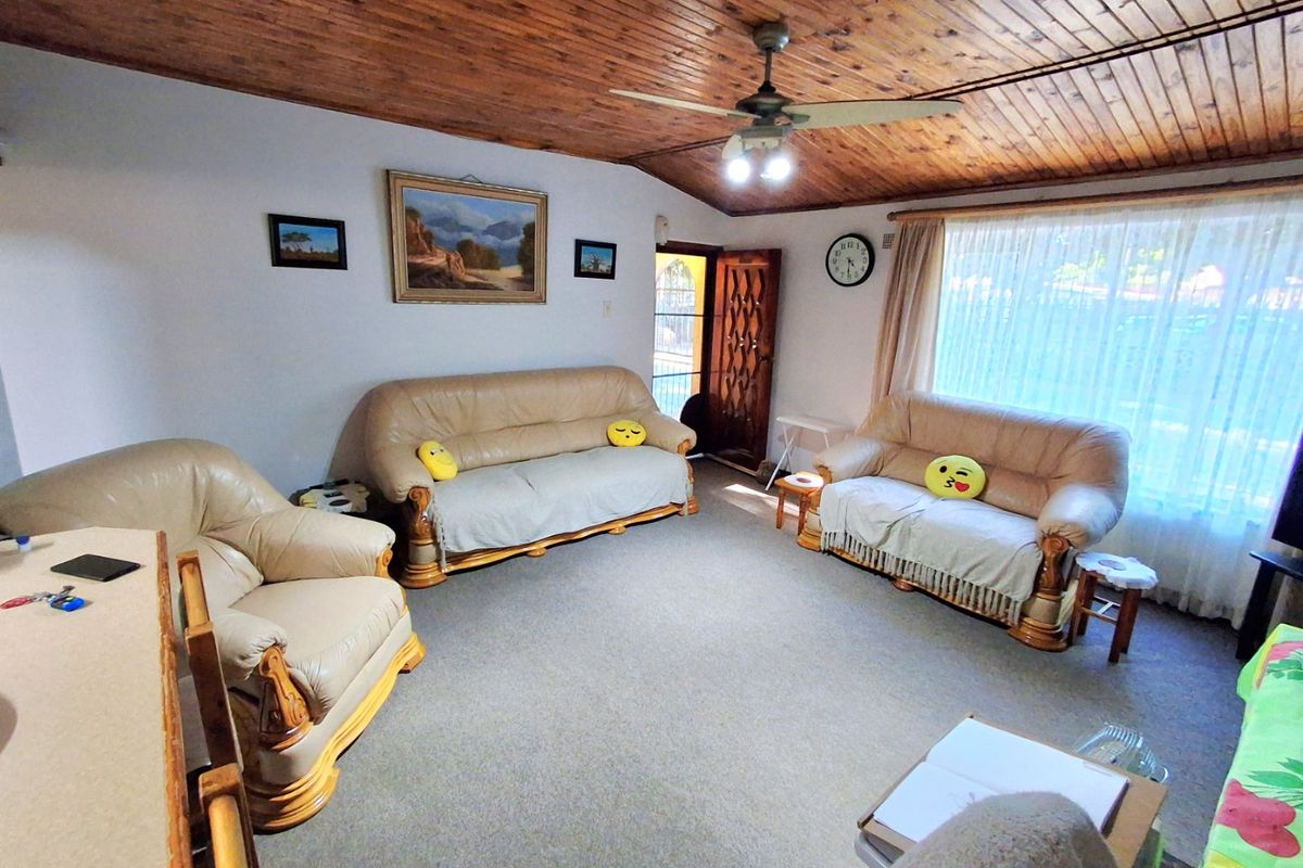 A living room featuring a timber tongue and groove ceiling, ceiling fan, and carpeted flooring with natural light from the window.