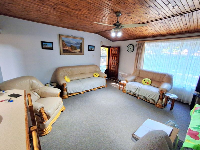 A living room featuring a timber tongue and groove ceiling, ceiling fan, and carpeted flooring with natural light from the window.