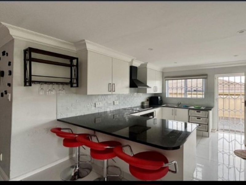 Modern kitchen featuring granite countertops, ample built-in cabinetry, a tiled backsplash, and direct access to an outdoor area through a security gate.