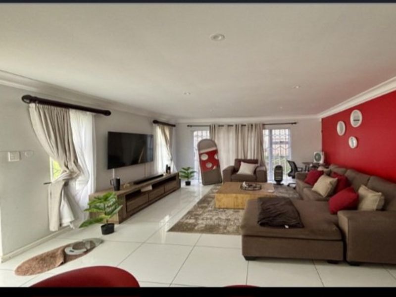 Spacious living room featuring large format floor tiles, recessed downlighting, and a prominent accent wall, providing a bright and open atmosphere.