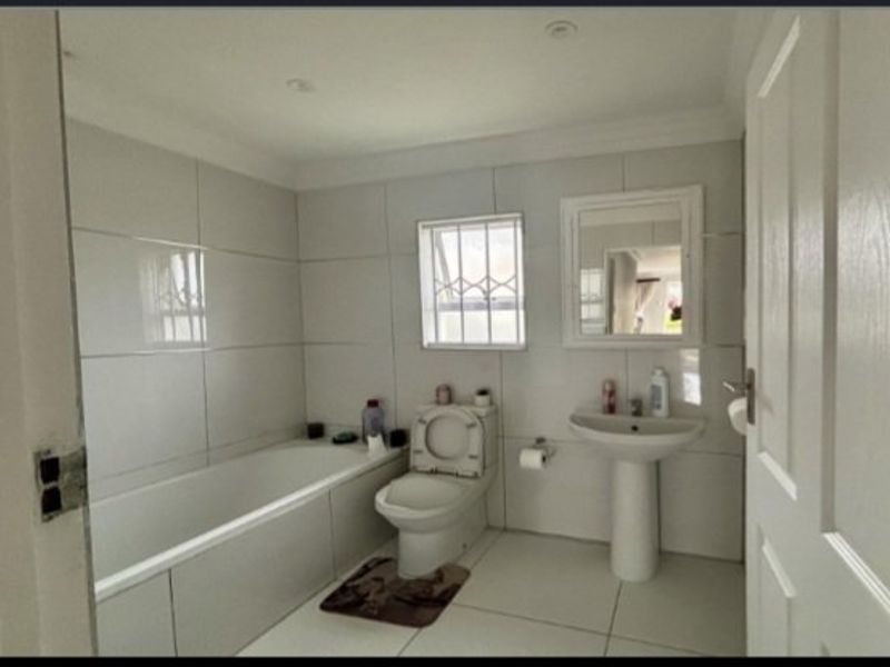 A clean, functional bathroom featuring a built-in bathtub, pedestal sink, toilet, and neutral wall and floor tiling with recessed lighting.