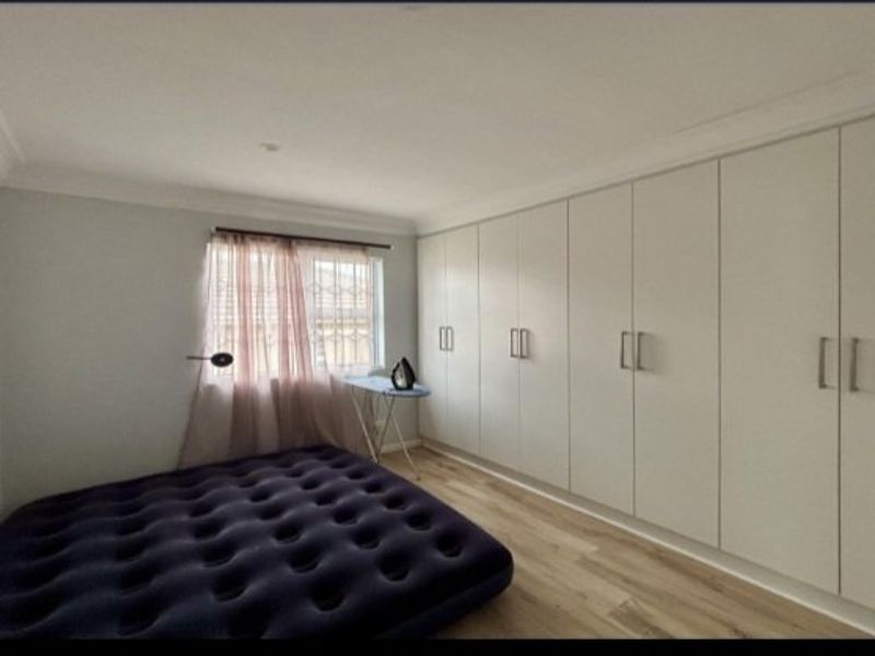 A bedroom featuring extensive built-in cupboards, laminate flooring, and security bars on the window.