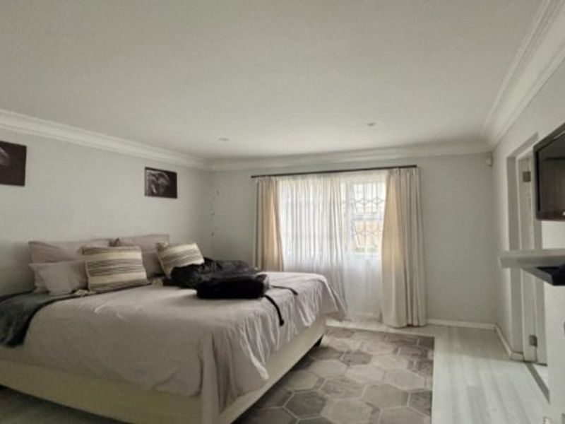 A spacious bedroom featuring neutral wall tones, cove cornicing, and light-toned laminate flooring, with a window fitted with a security gate.