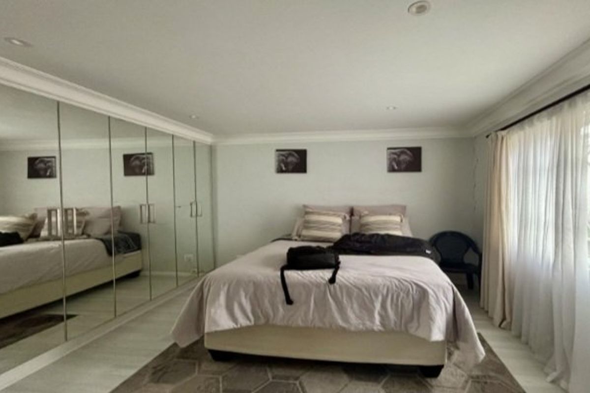 Spacious bedroom featuring extensive floor-to-ceiling mirrored built-in cupboards, recessed downlighting, and elegant crown molding, creating a bright and functional living space.