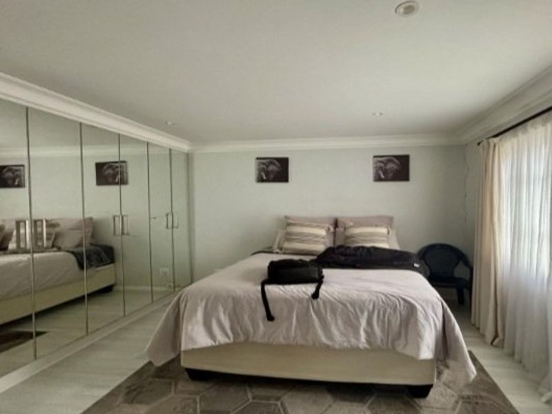 Spacious bedroom featuring extensive floor-to-ceiling mirrored built-in cupboards, recessed downlighting, and elegant crown molding, creating a bright and functional living space.