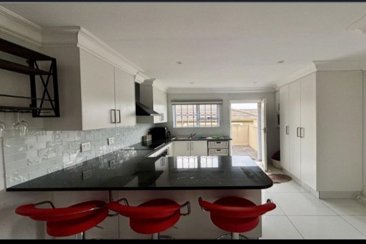 Modern kitchen featuring granite countertops, subway tile backsplash, ample built-in cabinetry, and direct access to an outdoor patio area.