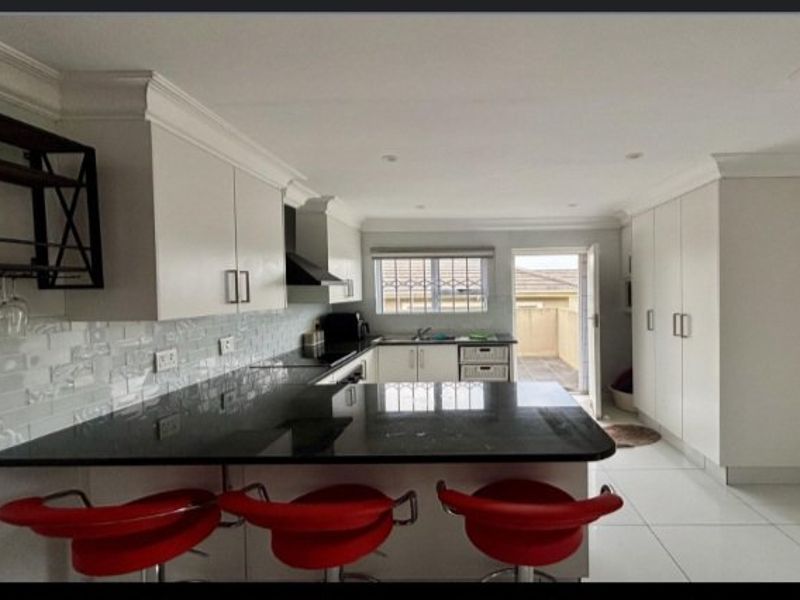 Modern kitchen featuring granite countertops, subway tile backsplash, ample built-in cabinetry, and direct access to an outdoor patio area.