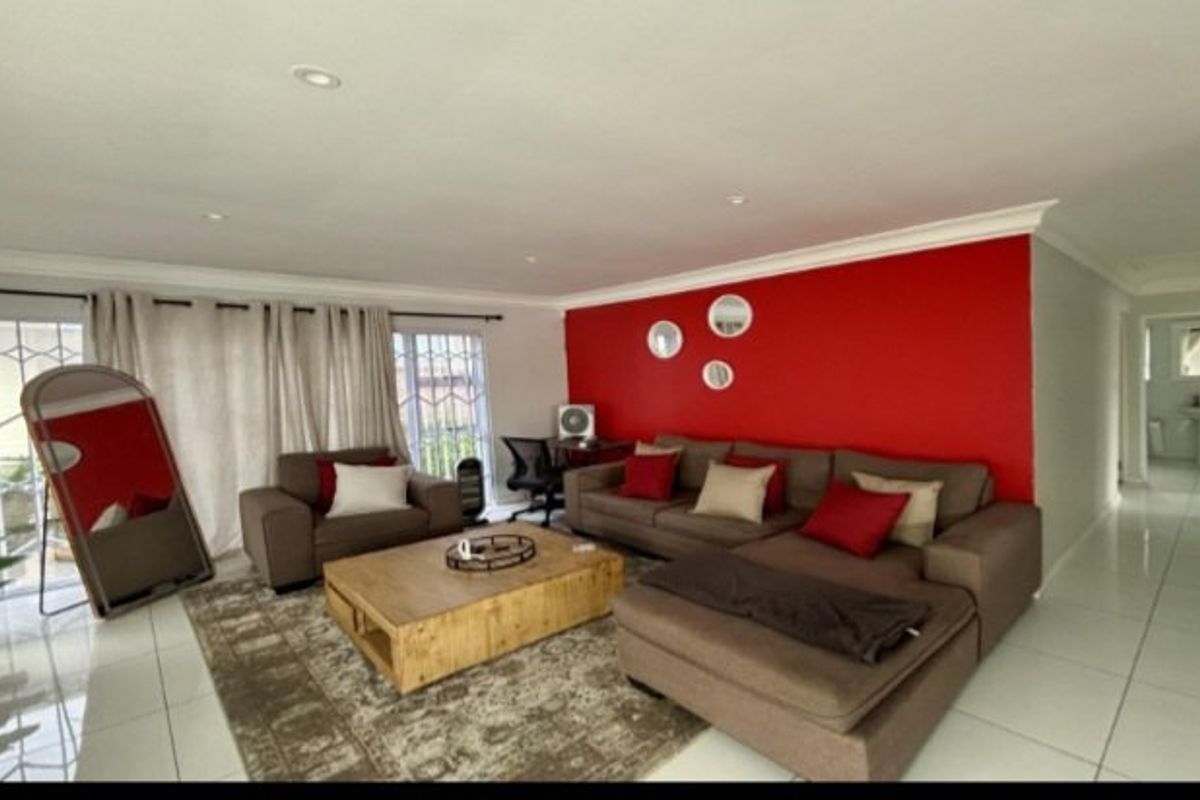 Spacious living room featuring tiled flooring, recessed downlighting, and a large sliding glass door with security gate, accented by a bold red feature wall.