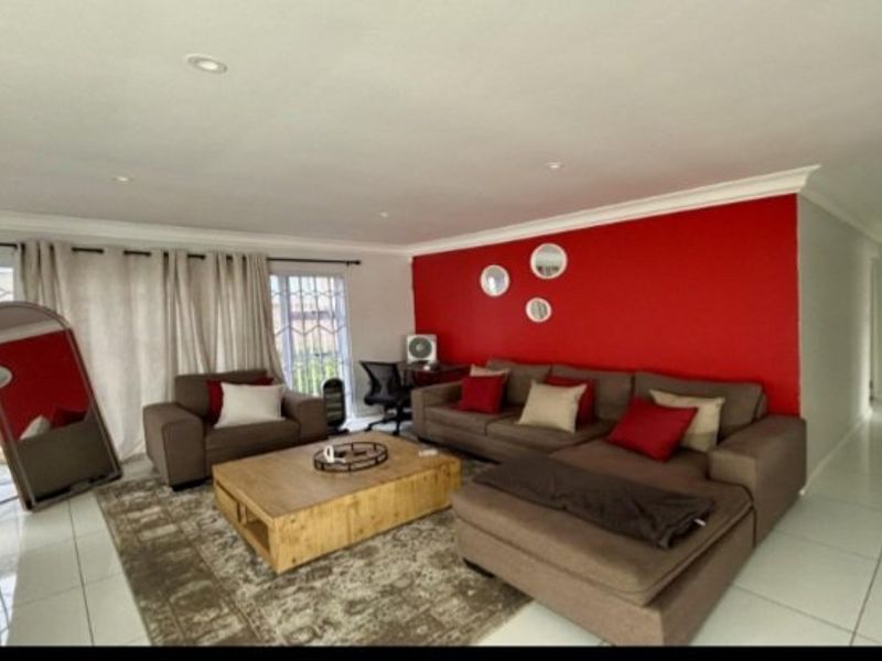 Spacious living room featuring tiled flooring, recessed downlighting, and a large sliding glass door with security gate, accented by a bold red feature wall.