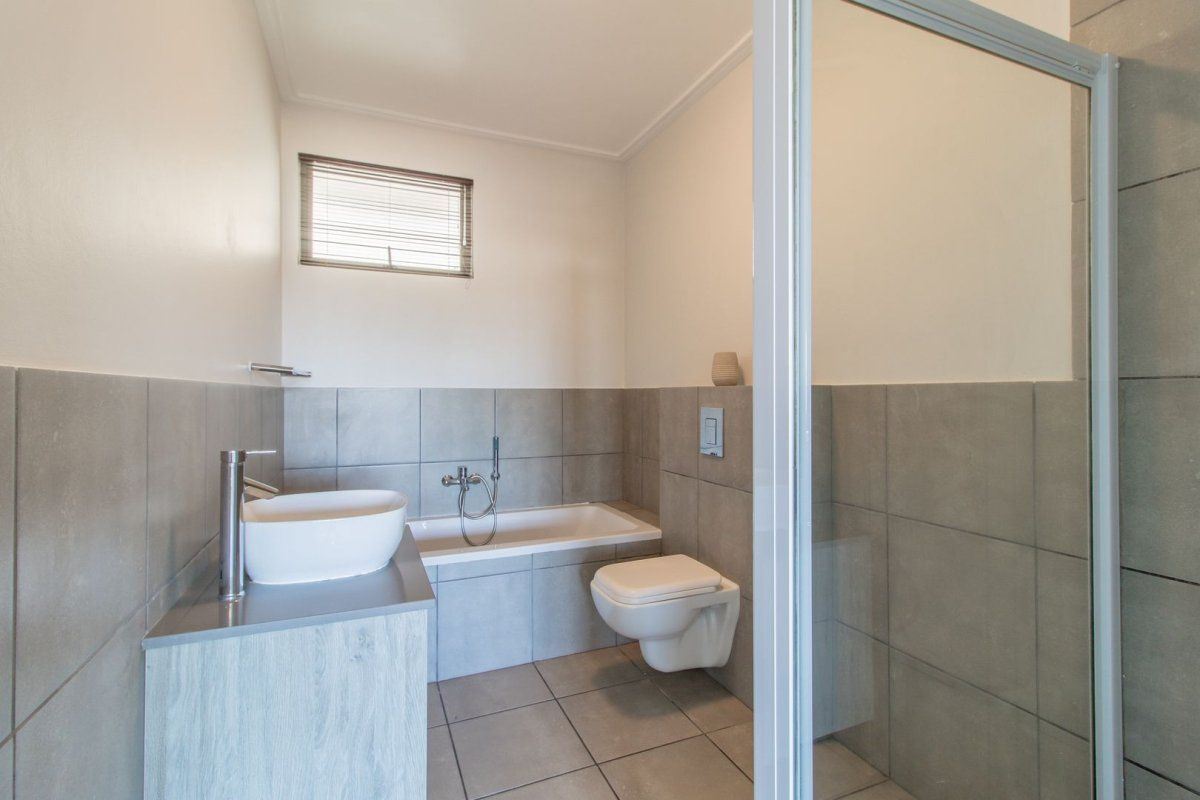 Modern bathroom featuring a wall-mounted toilet, built-in bathtub, glass shower enclosure, and a contemporary vessel sink set on a vanity cabinet.