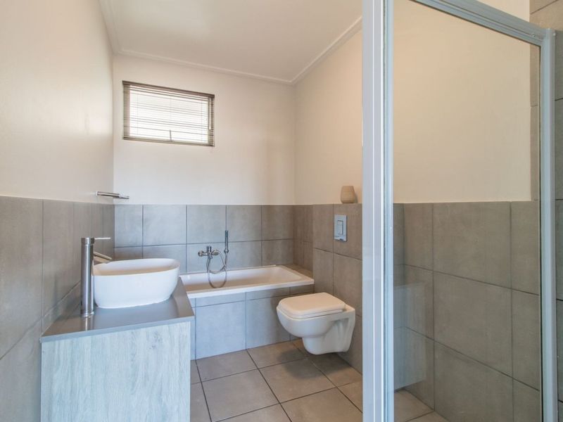 Modern bathroom featuring a wall-mounted toilet, built-in bathtub, glass shower enclosure, and a contemporary vessel sink set on a vanity cabinet.